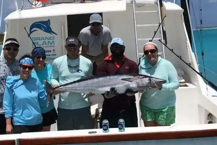 Group of people on a boat holding a large fish, with bright blue water in the background.