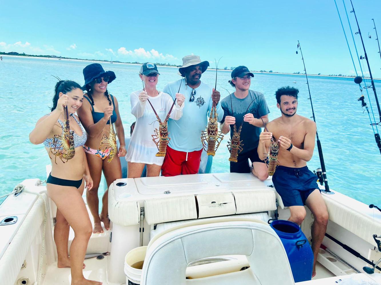 Six people on a boat holding lobsters, standing near fishing rods with a clear blue sea background.