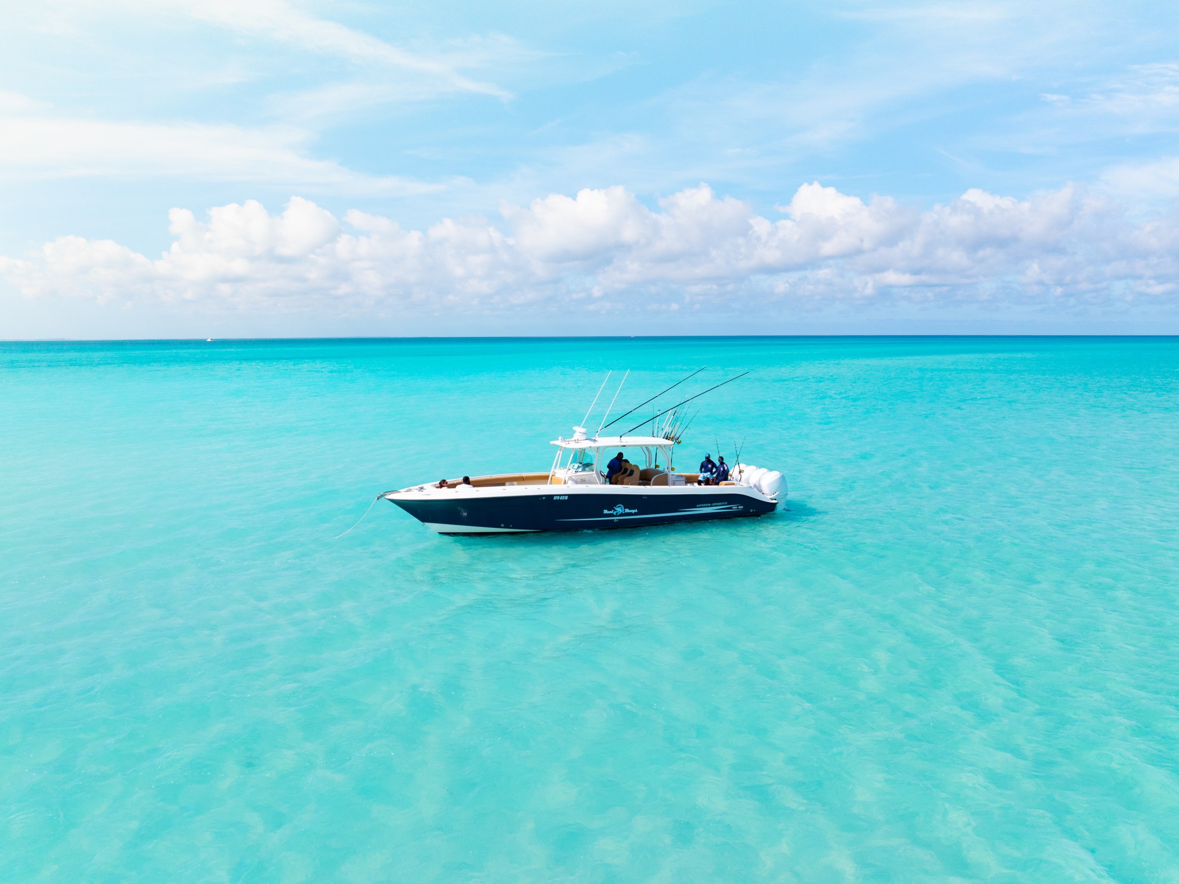 A boat floating on clear turquoise water under a blue sky with clouds.